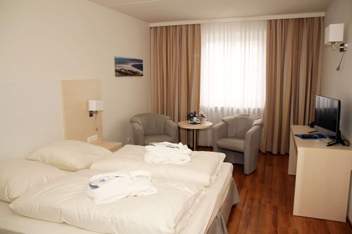 Een hotelkamer met een bed, twee fauteuils, een kleine tafel, een bureau met een televisie en gordijnen.