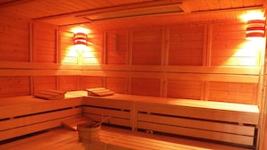 Una sauna con bancos de madera, un cubo de madera y dos luces fijadas a la pared.