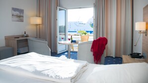 Habitación de hotel con cama, escritorio, silla, mesa con botella y vaso, y vista al mar y un barco.