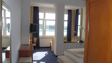 Ein Hotelzimmer mit Bett, Schreibtisch, Stuhl, Fernseher und Blick auf ein Gewässer durch die Fenster.