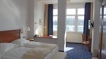 Habitación de hotel con una cama grande, un escritorio, una silla y vistas a un paisaje nevado a través de la ventana.