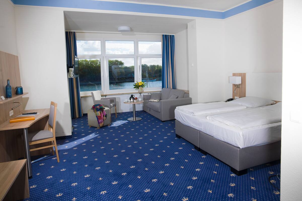 Een hotelkamer met een groot bed, een bureau, een stoel, een bank en uitzicht op een meer door de ramen.