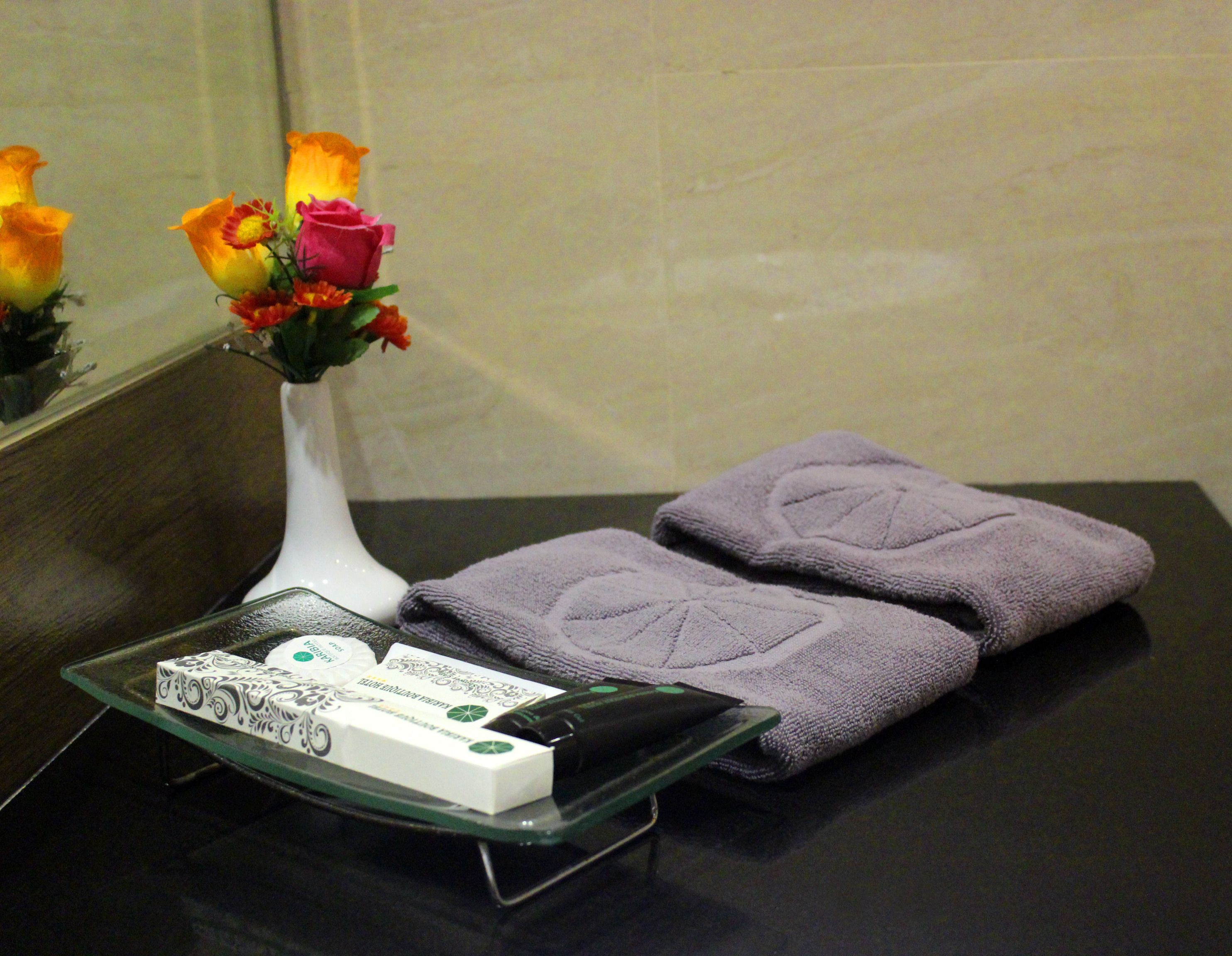 A bathroom with a glass tray holding toiletries, a vase with flowers, and folded towels on a dark countertop.