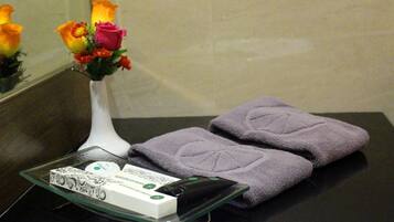 A bathroom with a glass tray holding toiletries, a vase with flowers, and folded towels on a dark countertop.