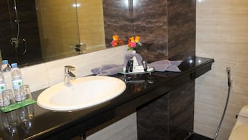 A bathroom with a white sink, dark marble countertop, and a mirror above it. There are toiletries on the counter and a showerhead visible.