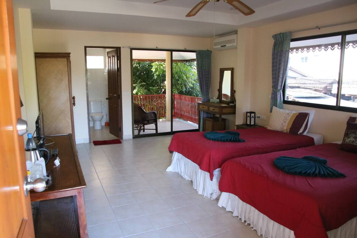 A hotel room with two beds, a desk, a chair, a bathroom, and a balcony with a red railing.