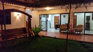 Un patio con un banco de madera, dos sillas de mimbre y una planta en maceta.