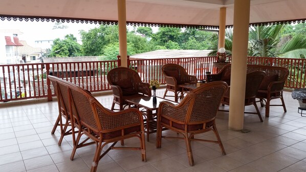 A covered outdoor seating area with wicker furniture and a view of a residential street. - Villa Oranje (Chiang Mai)