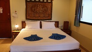 Habitación de hotel con cama, mesita de noche con lámpara, tapiz en la pared y ventana con cortinas.