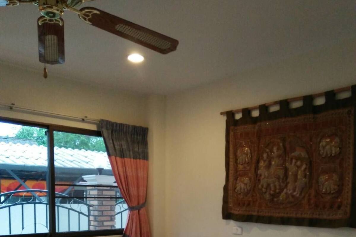 A hotel room with a bed, a ceiling fan, a window with curtains, and a wall-mounted artwork.