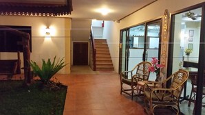 Amplio espacio interior con una escalera que lleva a un nivel superior, una zona de estar con sillas de mimbre y un pequeño jardín con una planta.