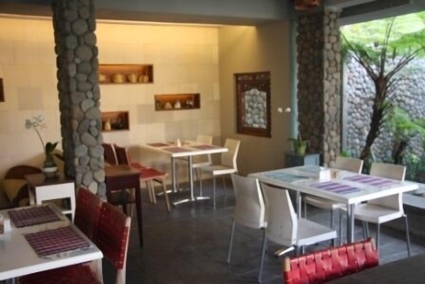 A dining area with white tables and chairs, stone pillars, and a view of greenery outside.