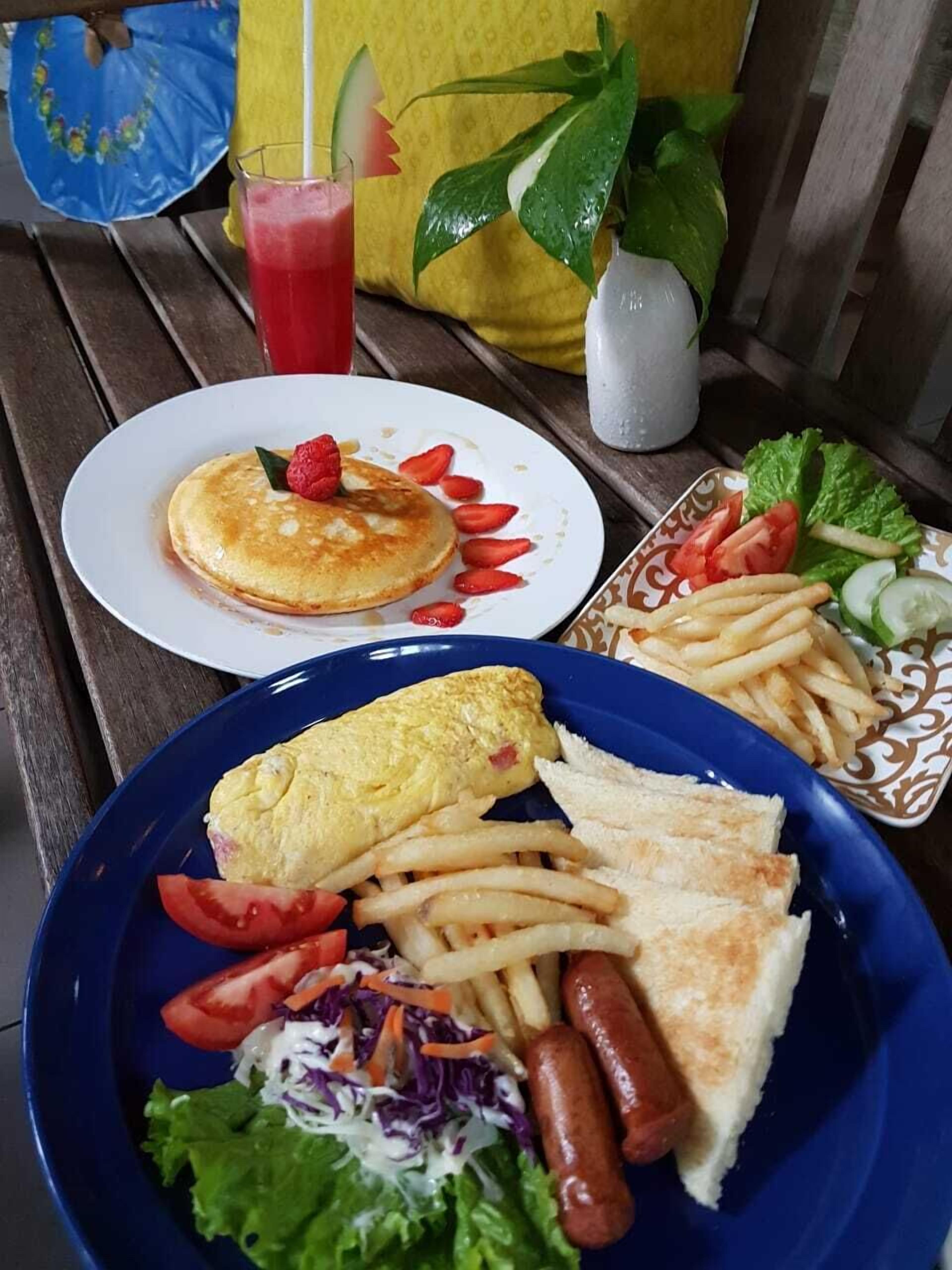 A meal consisting of pancakes, French fries, sausages, a salad, and an omelet on a wooden table.