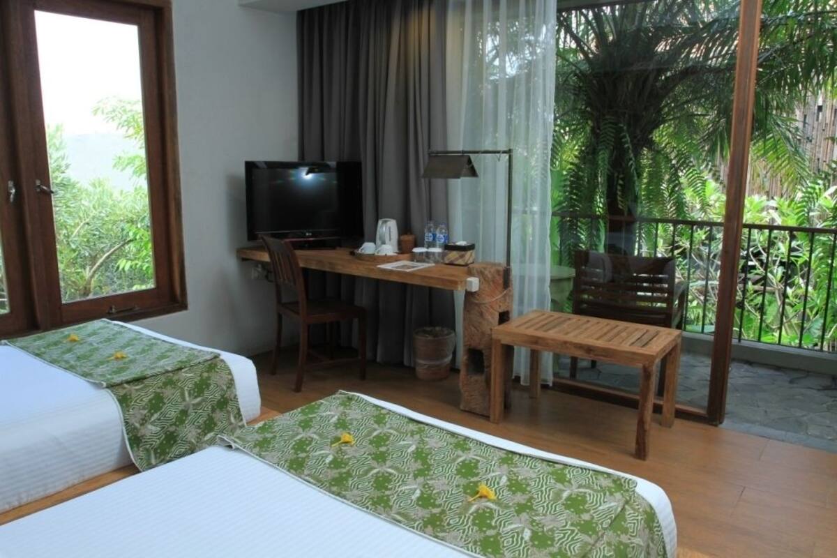 Een hotelkamer met twee bedden, een bureau met televisie en een balkon met uitzicht op groen.