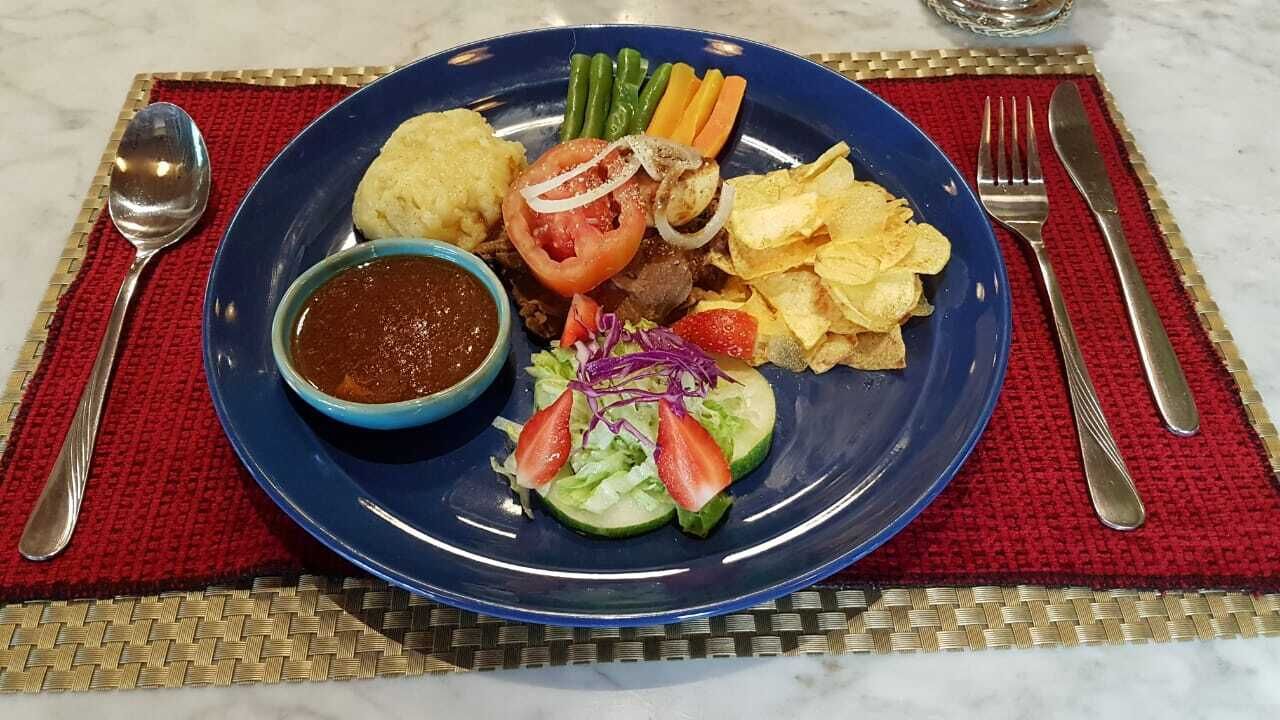 Um prato com uma variedade de alimentos, incluindo salada, batatas fritas e uma pequena tigela de molho, apoiado em um jogo americano vermelho.