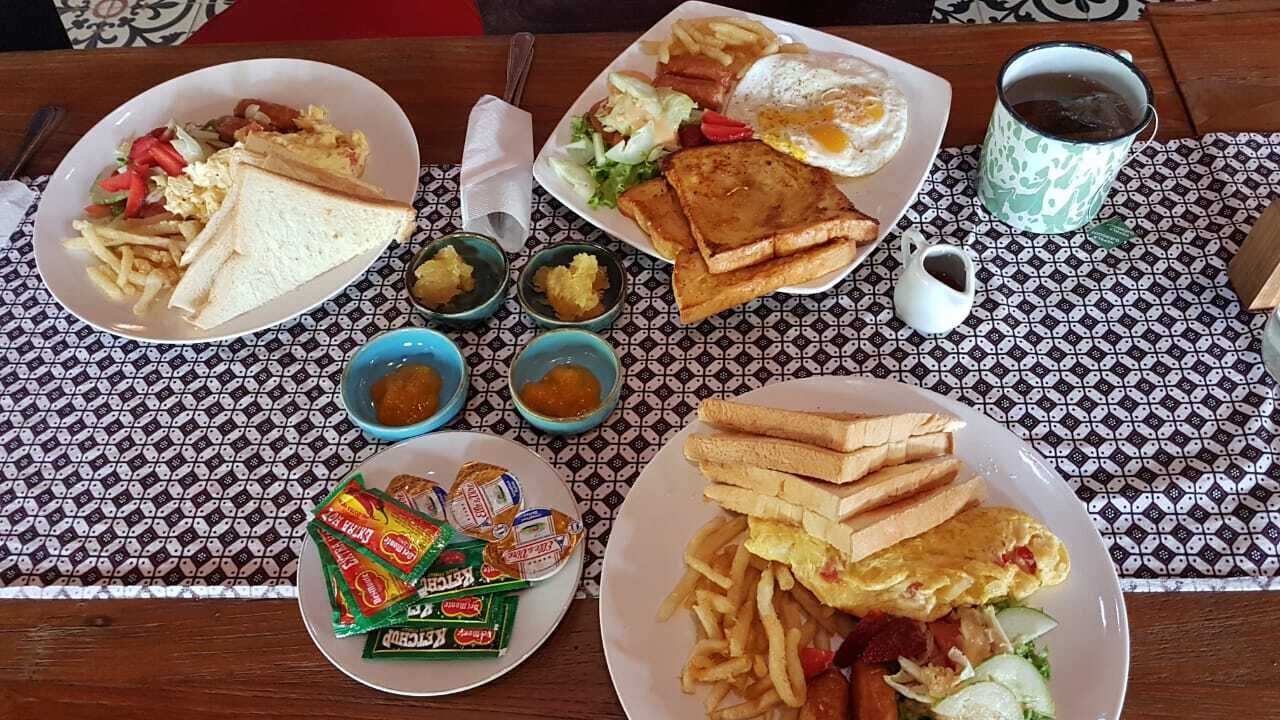 Una mesa con platos de comida que incluyen sándwiches, papas fritas y huevos. Hay recipientes pequeños con salsas y una taza de café.