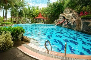 A swimming pool with a waterfall feature, surrounded by tropical vegetation and a gazebo. - Hotel Puri Asri (Magelang)