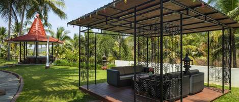 Un espacio de estar al aire libre cubierto con una terraza de madera, rodeado de exuberante vegetación y palmeras.