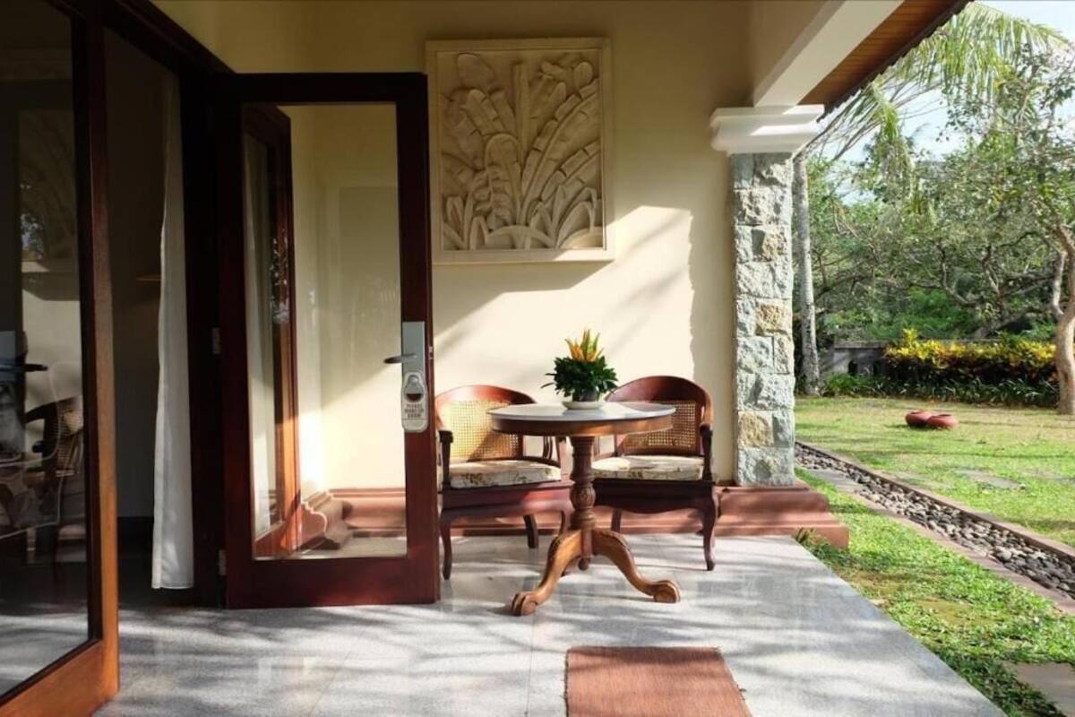 A room with a wooden door, a round table with chairs, a wall-mounted artwork, and a stone pillar.