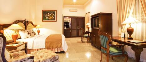 A hotel room with a bed, two bedside tables with lamps, a chair, a desk with a lamp, a wardrobe, and a painting on the wall.