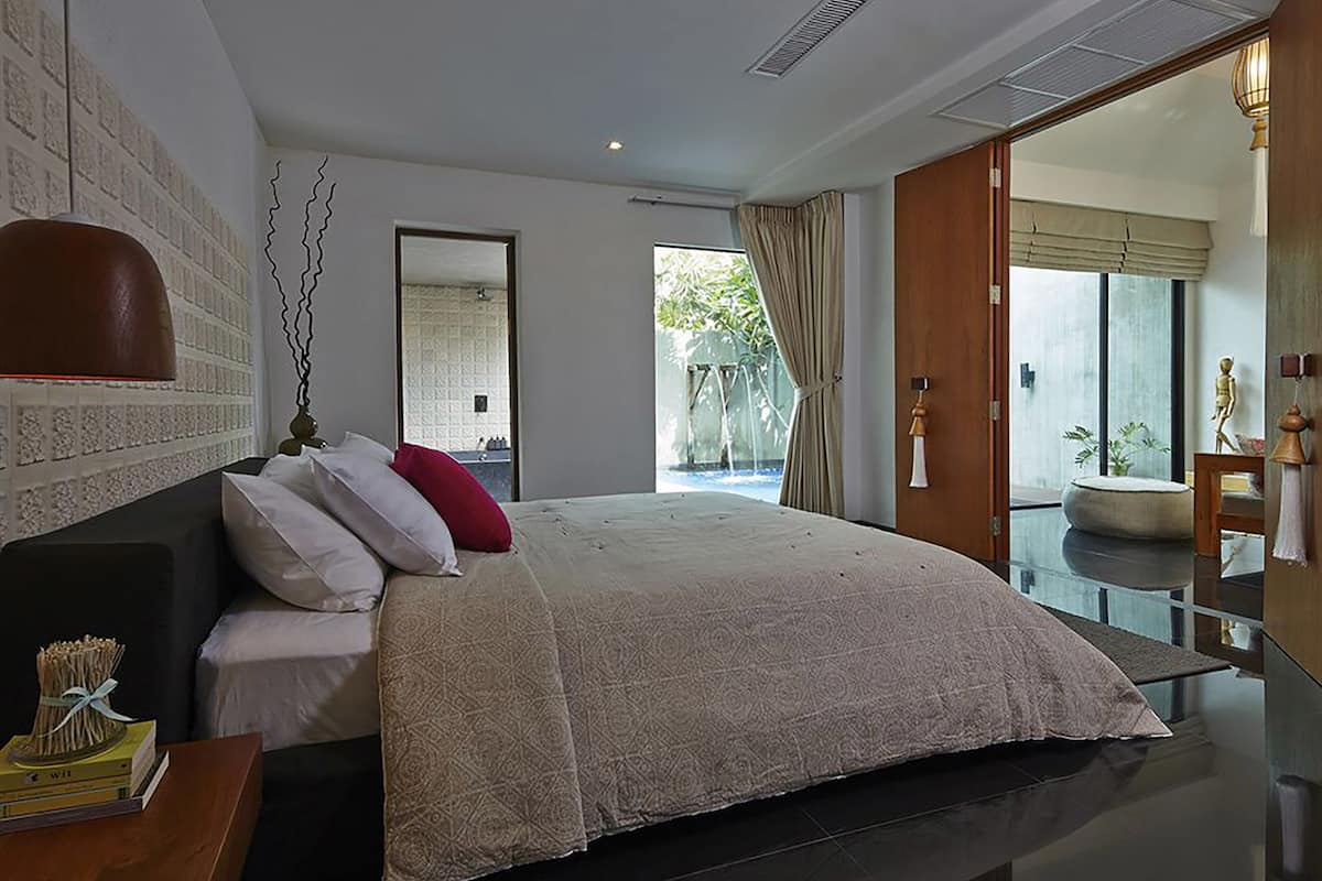 Ein modernes Schlafzimmer mit einem großen Bett, einem Nachttisch aus Holz, einem Spiegel und Blick auf einen Garten durch das Fenster.