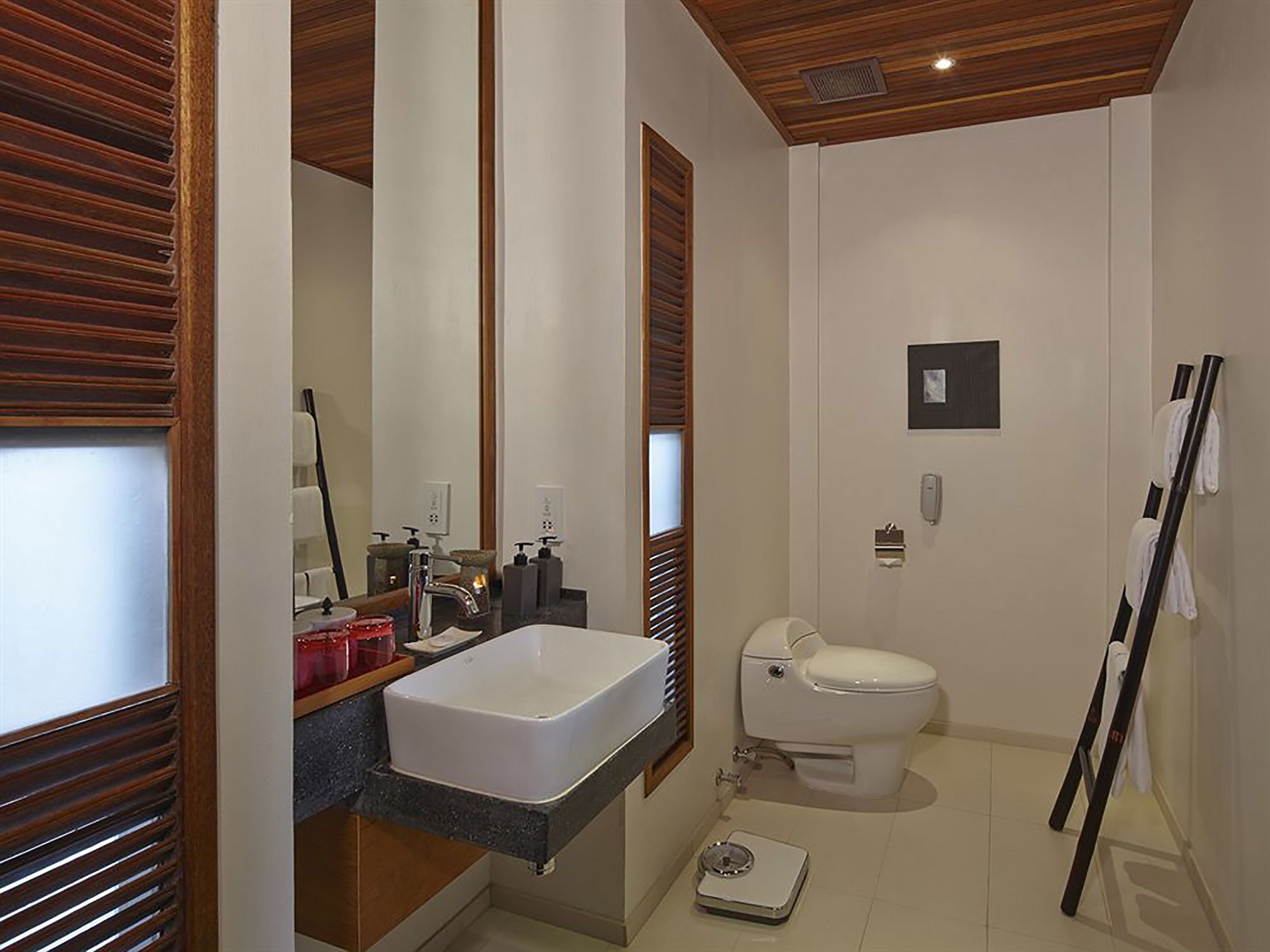 A modern bathroom with a large mirror, a white sink, a toilet, and a towel rack.