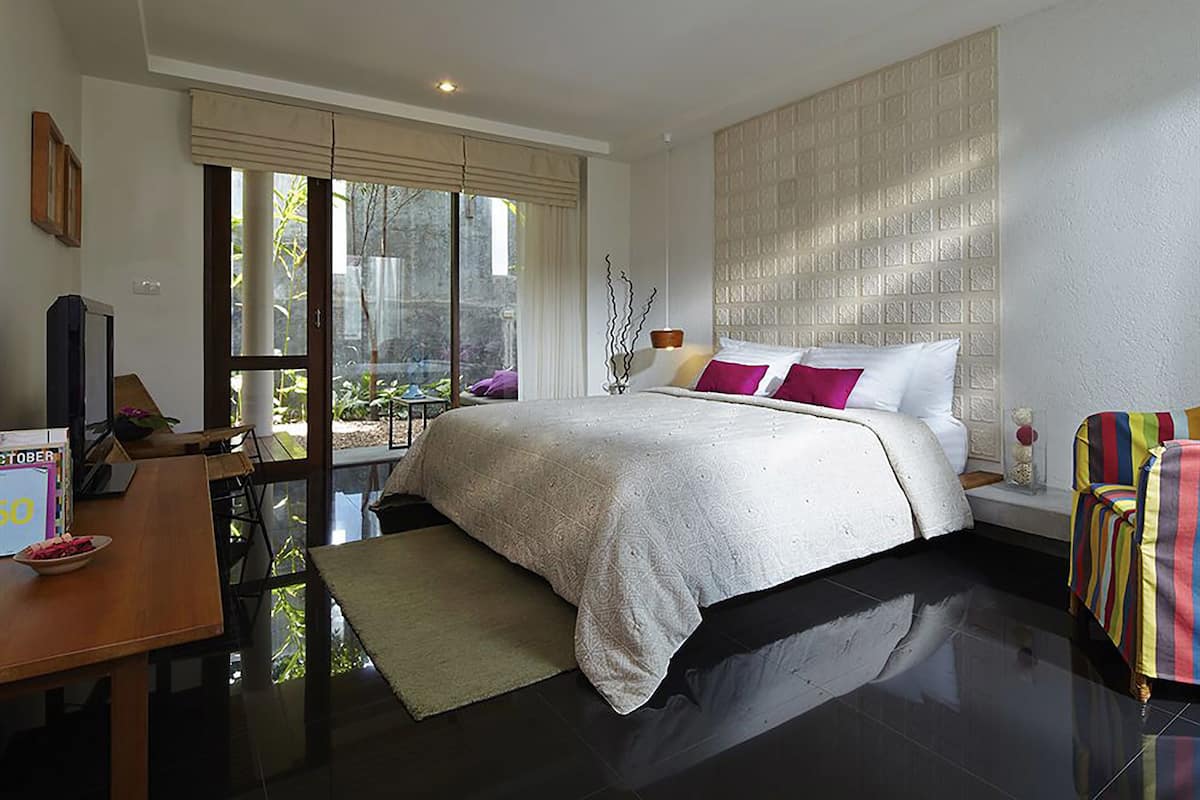 Ein modernes Hotelzimmer mit einem großen Bett, einem Schreibtisch mit Computer, einem Stuhl und einem Fenster mit Blick auf Grünflächen.