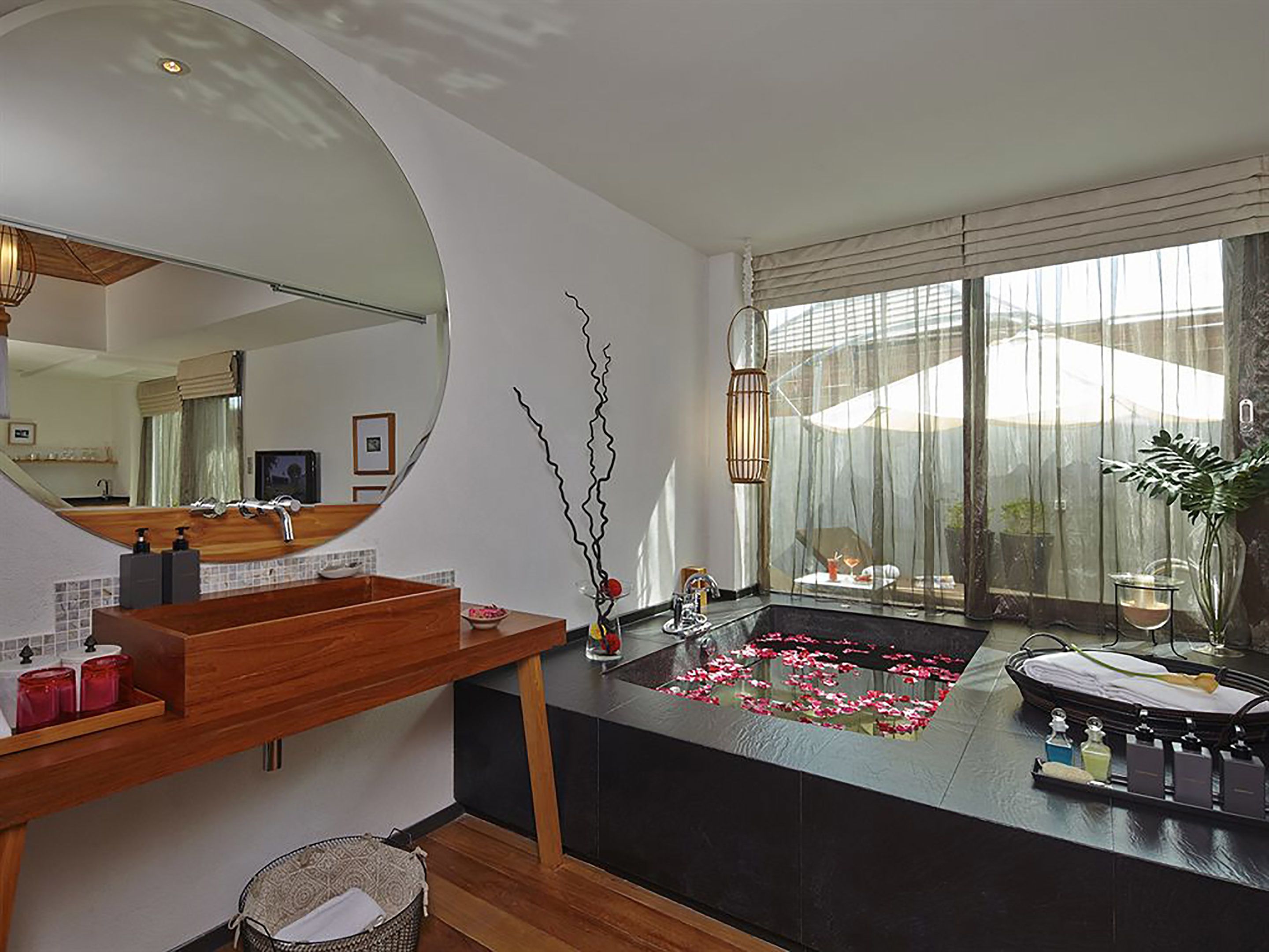 Un baño moderno con un espejo grande, tocador de madera y una bañera negra con un arreglo floral decorativo.