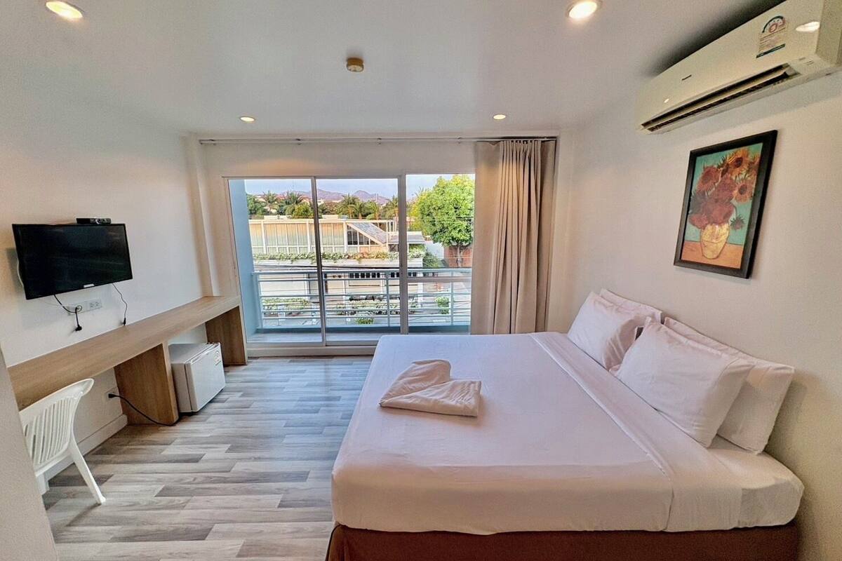 Ein Hotelzimmer mit Bett, Fernseher, Schreibtisch und Fenster mit Blick auf Gebäude und Bäume.