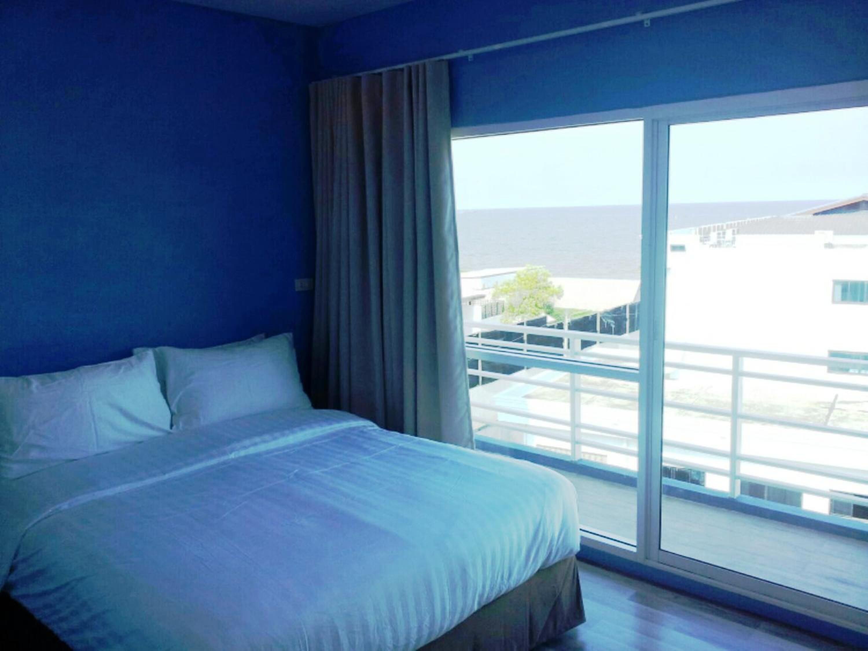 A hotel room with a large bed, a view of the sea, and a balcony with a railing.