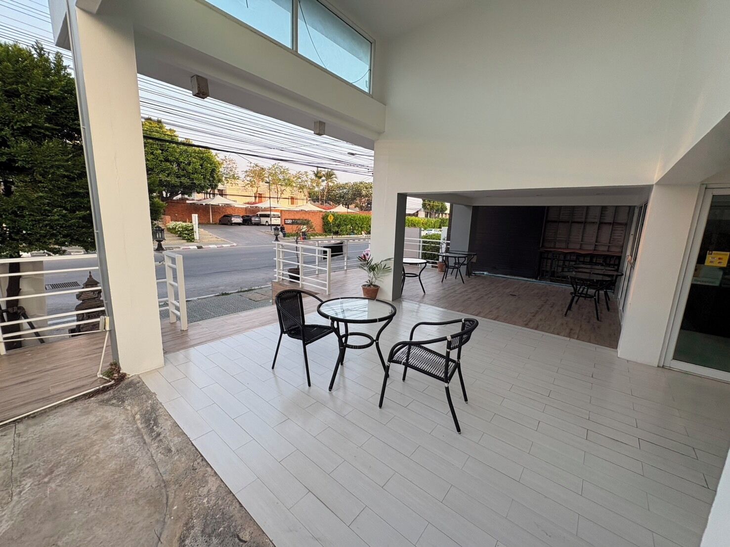 A modern outdoor patio with a round table and chairs, a fire pit, and a view of the street and greenery.