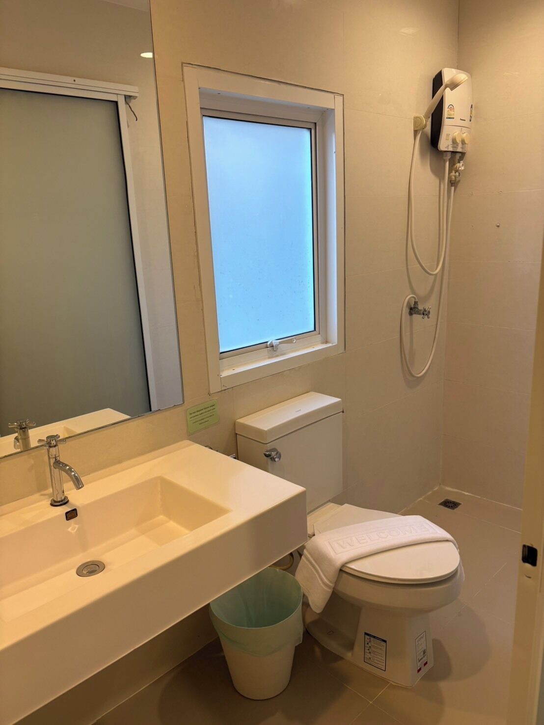 A bathroom with a sink, toilet, window, and shower.