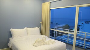 A hotel room with a large bed, white bedding, and a view of the city through a balcony. - Nantra Huahin (Hua Hin)