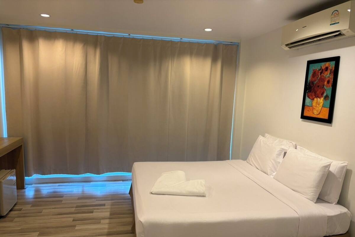 Ein Hotelzimmer mit Bett, Schreibtisch, einem fensterbelaubten Fenster, einer Klimaanlage und einem Bild an der Wand.