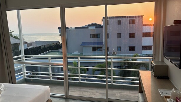 A hotel room with a large sliding glass door leading to a balcony with a view of the sea and buildings. - Nantra Huahin (Hua Hin)