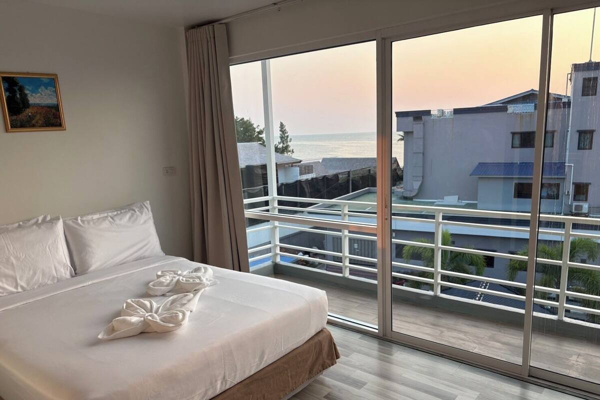 Ein Hotelzimmer mit Bett, einem Bild an der Wand und einem Balkon mit Blick auf Gebäude und das Meer.