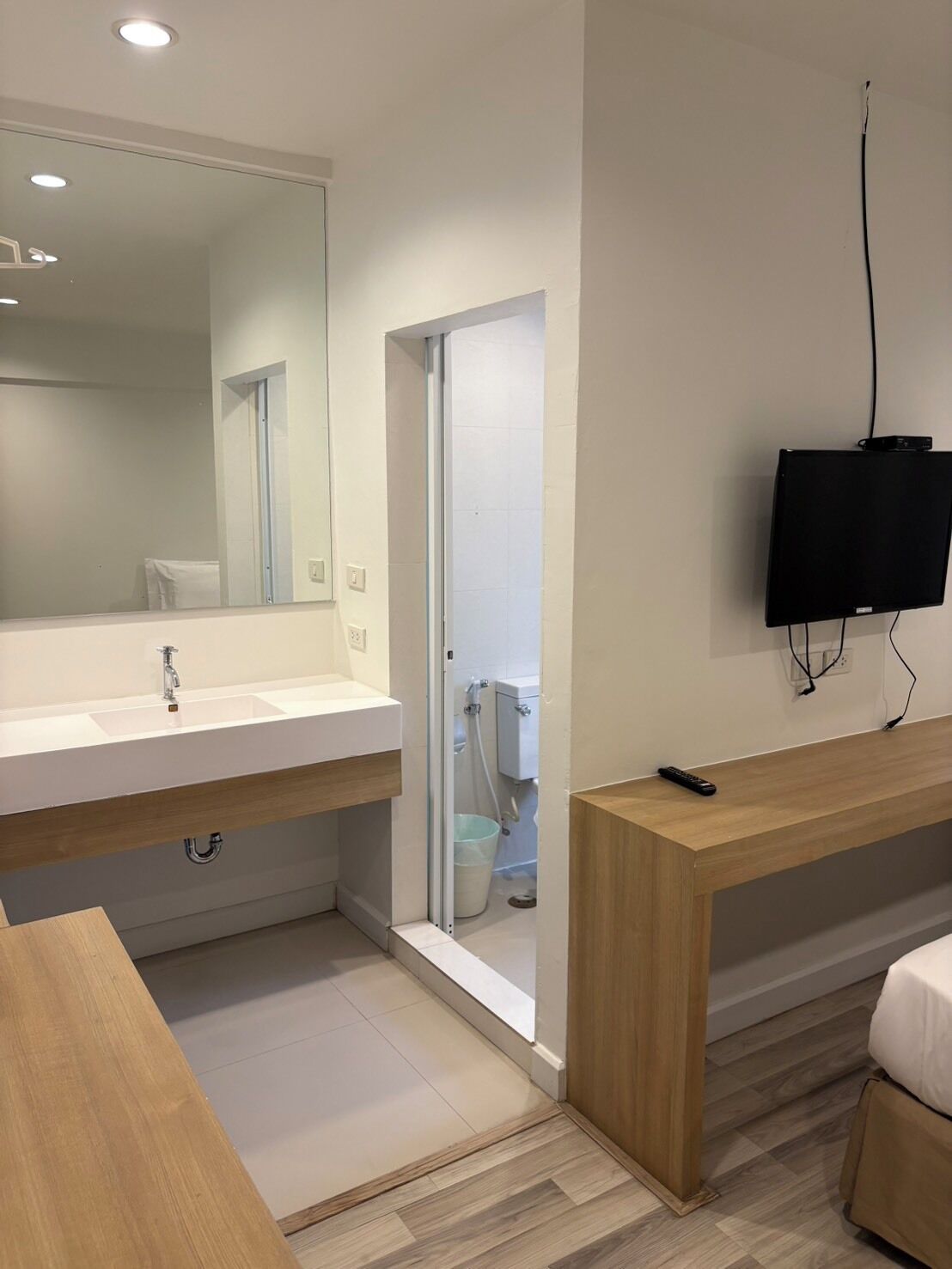Een moderne badkamer met een grote spiegel, twee wastafels, een toilet en een aan de muur bevestigde televisie.