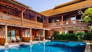 A pool area with a wooden building, outdoor seating, and a clear blue pool.