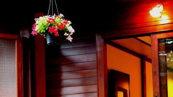 A wicker chair by a poolside, wooden walls, and a hanging flower basket.
