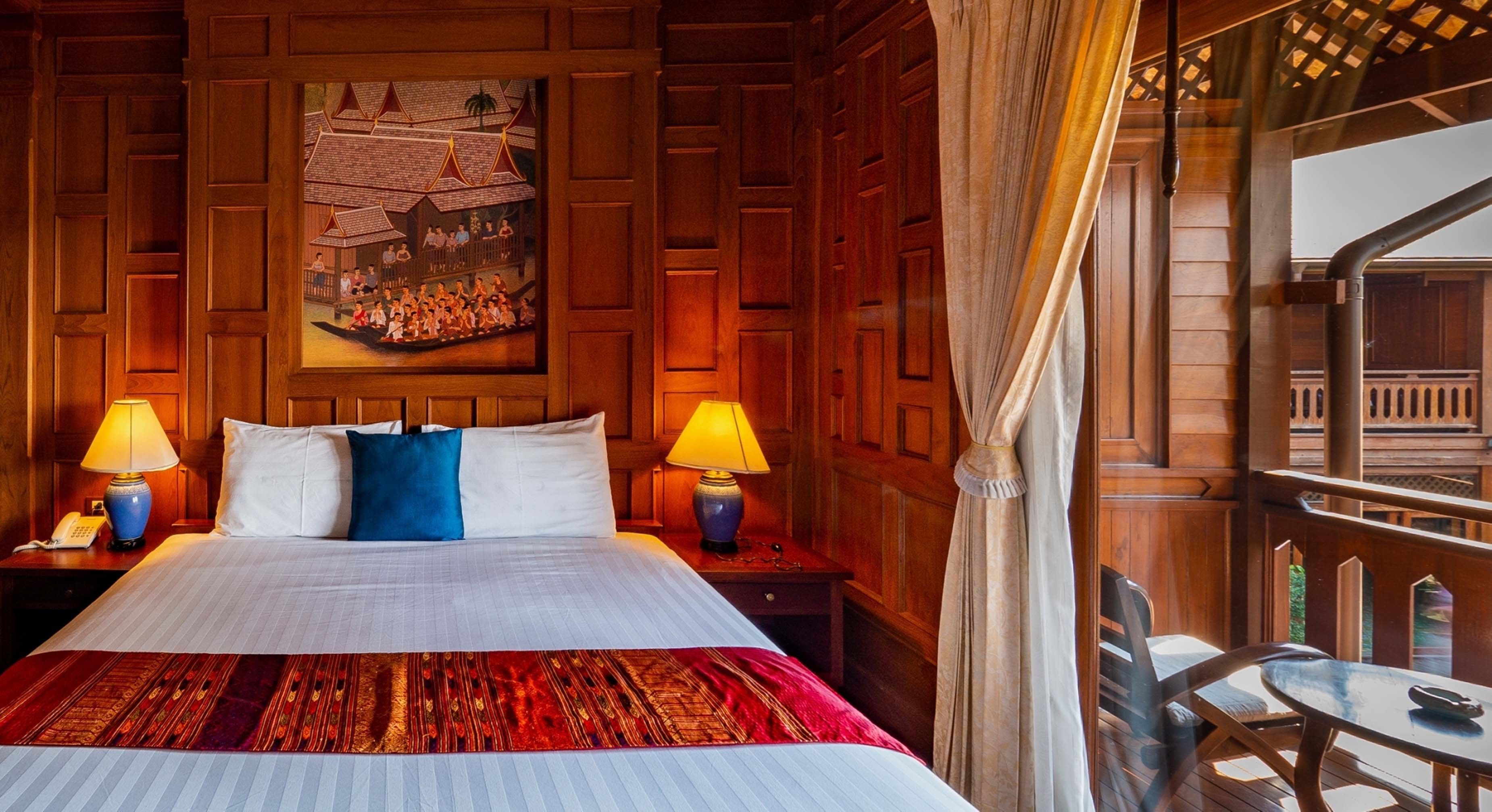 Habitación de hotel con una cama grande, dos lámparas de noche, un cabecero de madera, un cuadro de una escena tradicional y un balcón con vistas.
