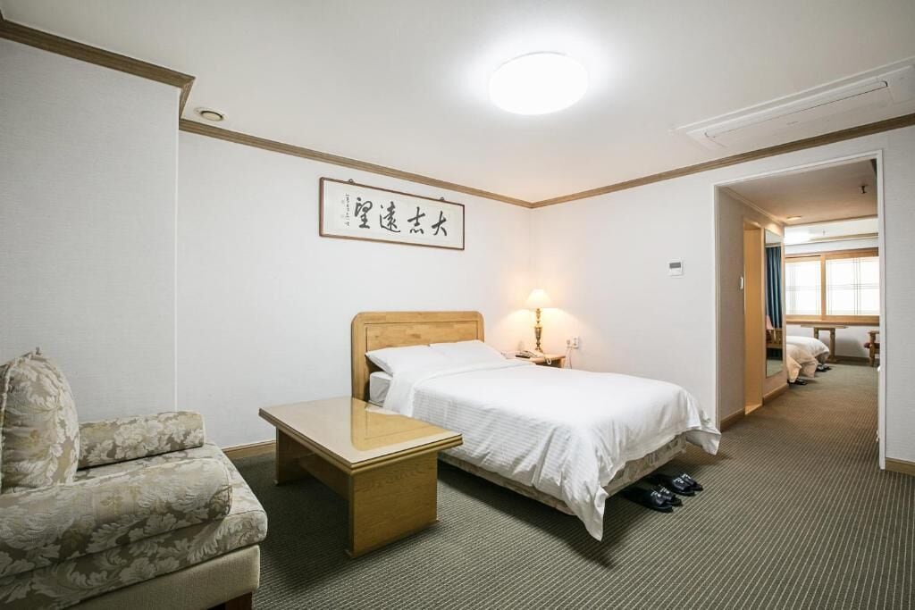 Une chambre d’hôtel avec un lit, une table de chevet et une chaise. Un tableau encadré est accroché au mur et une lampe se trouve sur la table de chevet.