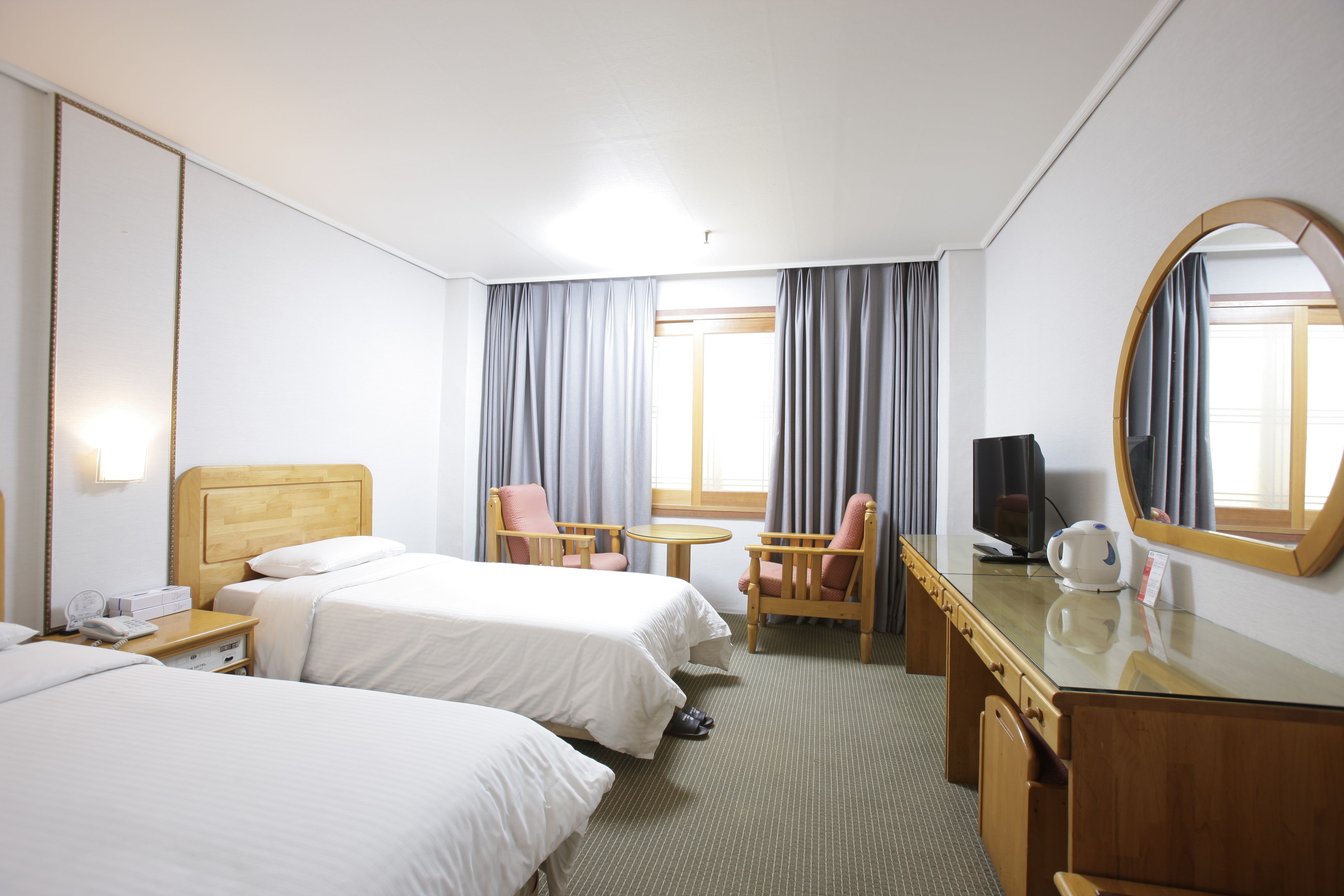 A hotel room with two beds, a desk, a chair, a TV, and a mirror.