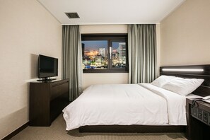 A hotel room with a bed, a TV, a desk, and a window with a city view. - Busan Tourist Hotel (Busan)