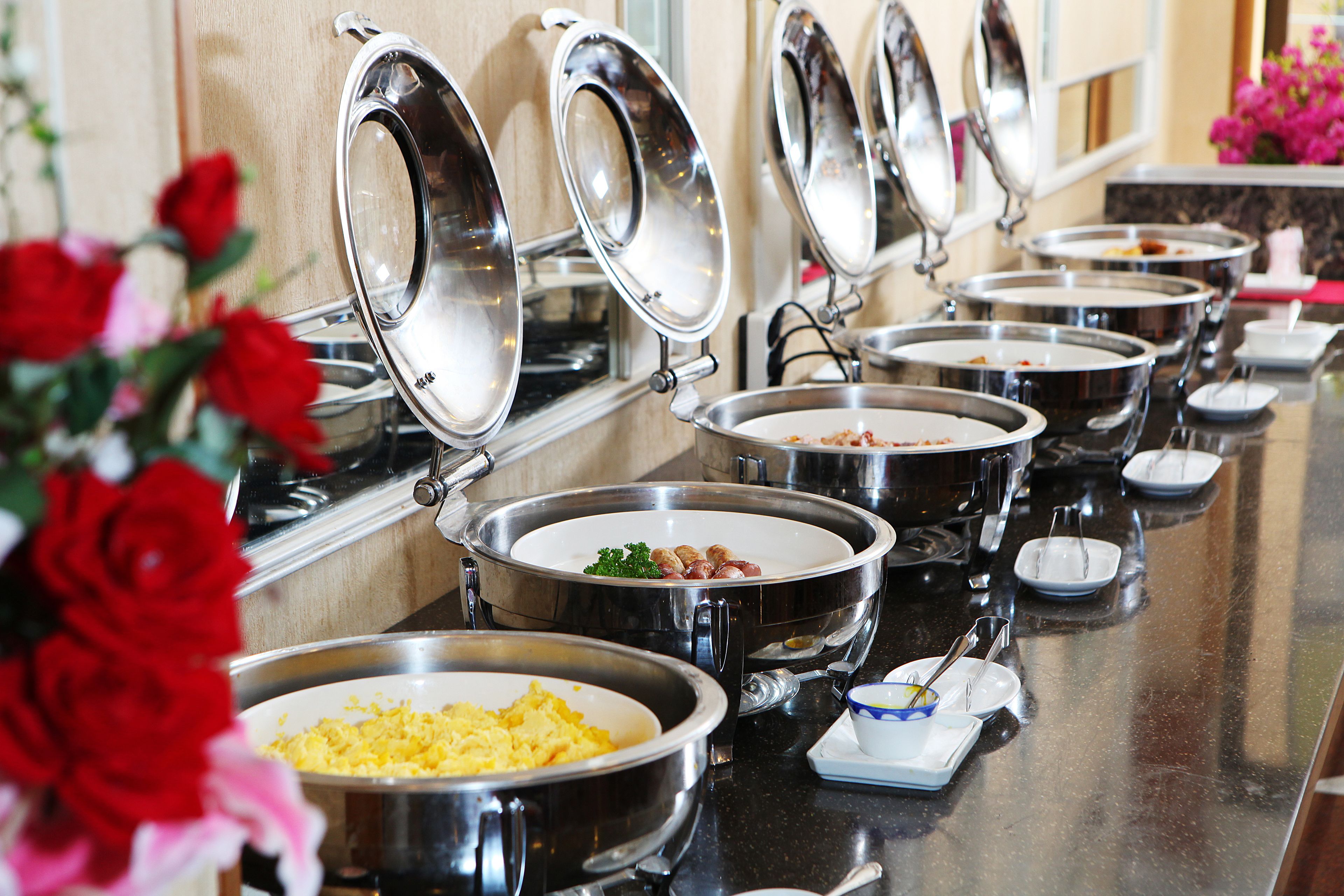 A buffet setup with multiple stainless steel serving dishes, each with a lid, arranged on a counter.