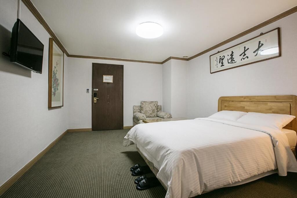 A hotel room with a bed, a chair, a television, and a door.