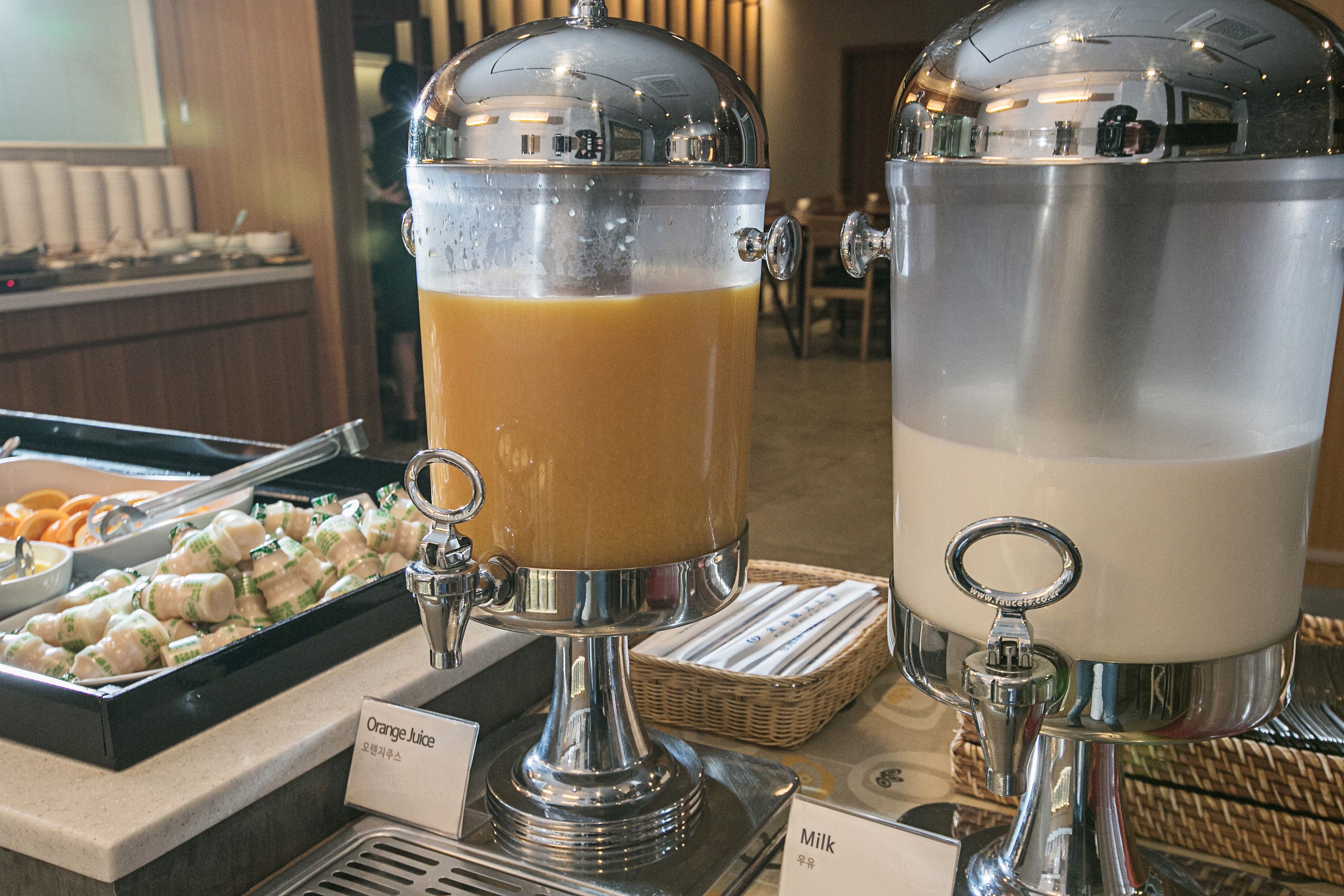A buffet with self-serve dispensers for orange juice and milk.