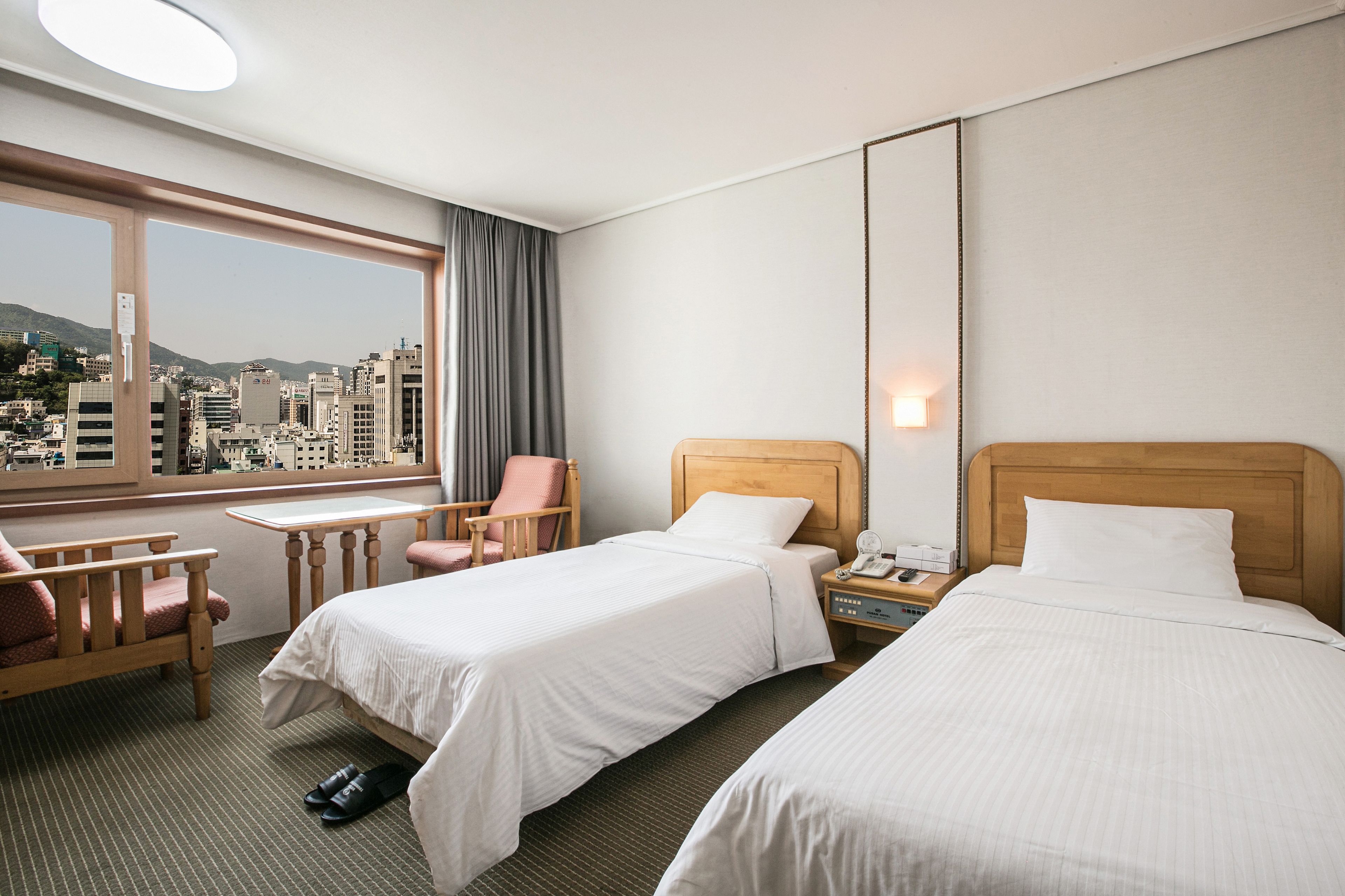 Habitación de hotel con dos camas, un escritorio, una silla y vistas a la ciudad.
