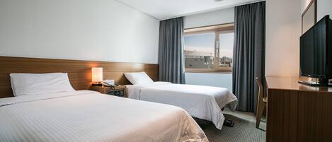 Una habitación de hotel con dos camas, un escritorio, un televisor y una ventana con cortinas.