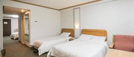 Habitación de hotel con dos camas, una mesita pequeña, una silla y un espejo.
