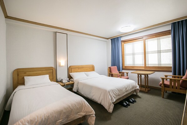 Habitación de hotel con dos camas, una mesita, una silla y un ventanal con cortinas.